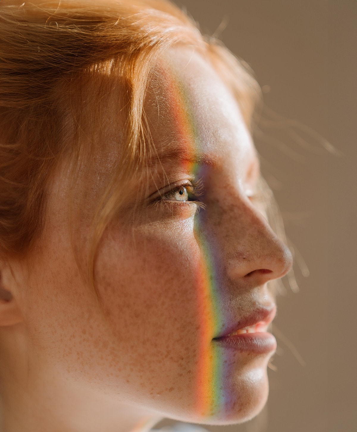 Woman's face with rainbow reflection on skin.
