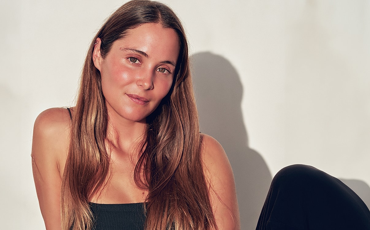 Woman with long hair posing against a wall.