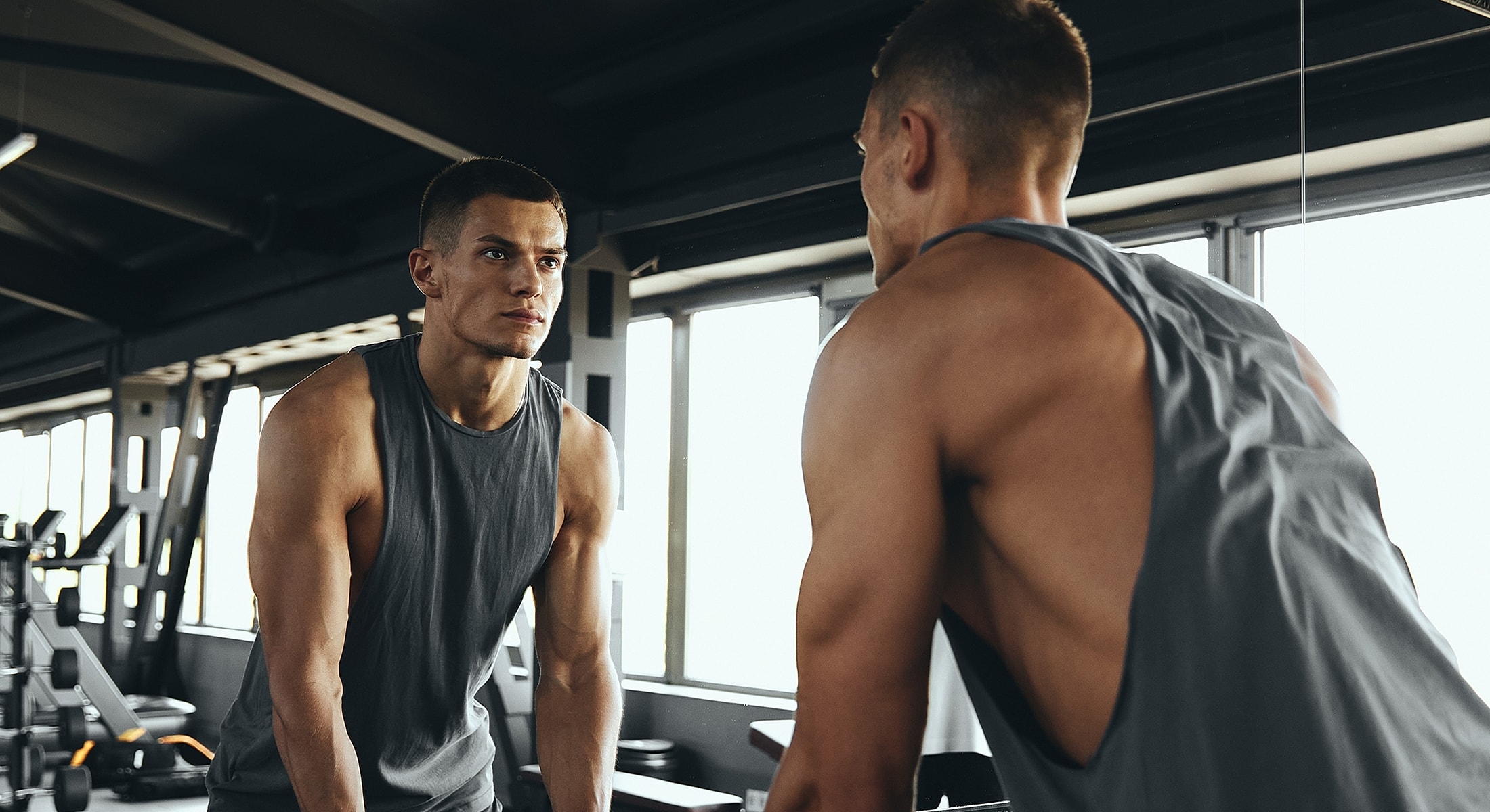 Man working out in gym, looking in mirror.