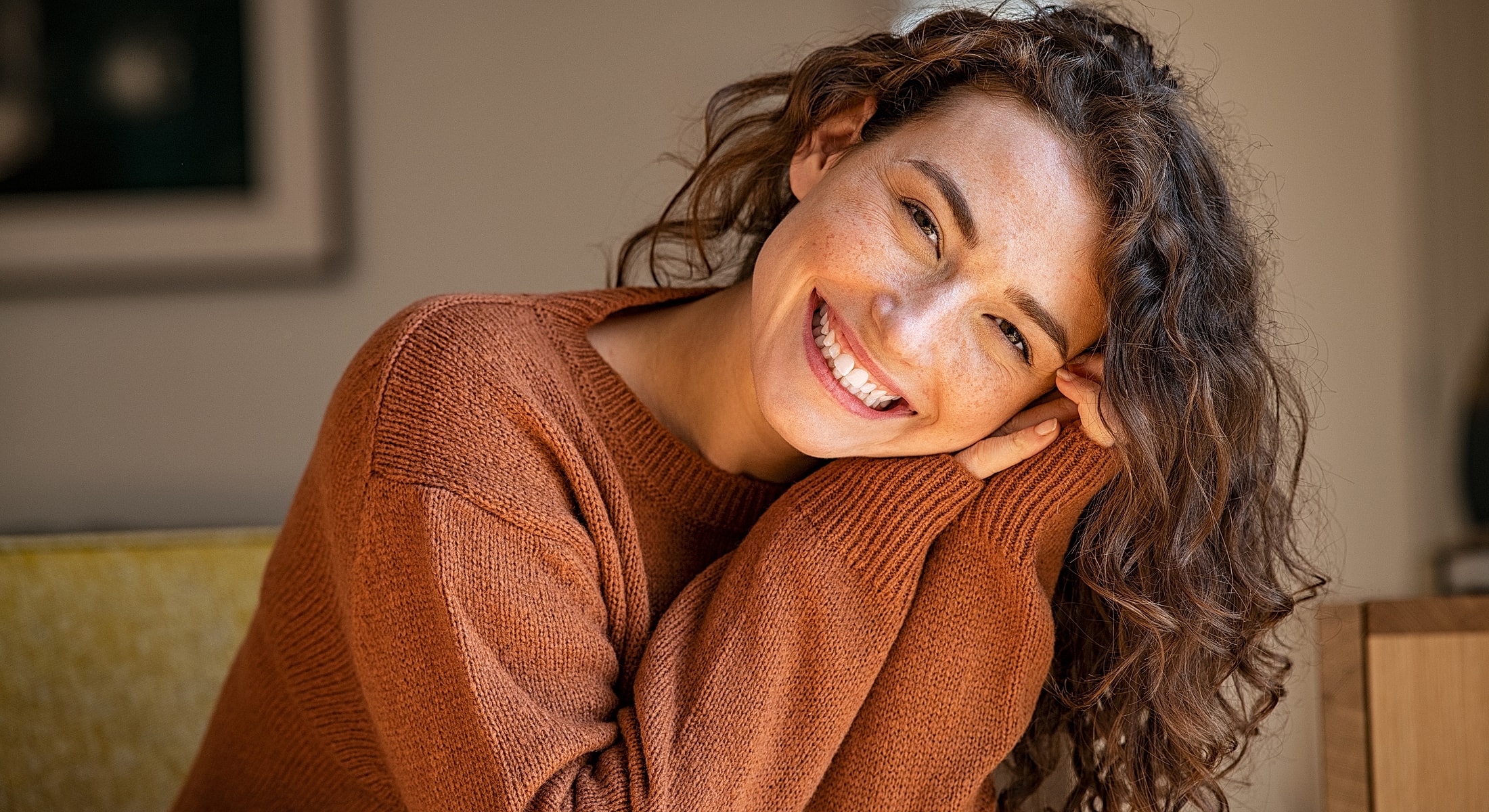 Smiling person with curly hair in cozy sweater.